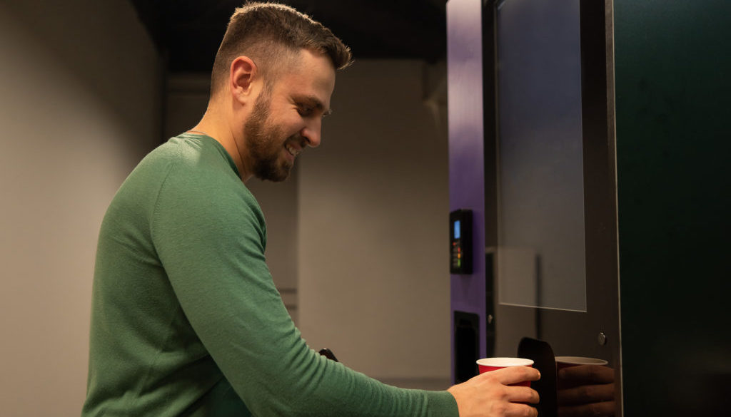 Caucasian Man Pours Himself Coffee From A Vending Machine.