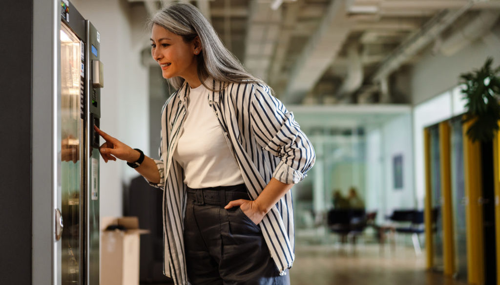 Happy white-haired mature woman using vending machine and smilin